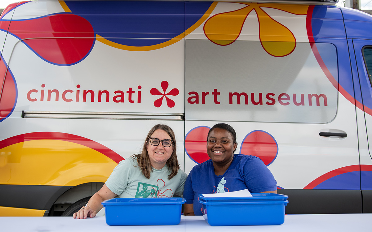 Two women smile at a table outside the CAM Cruiser
